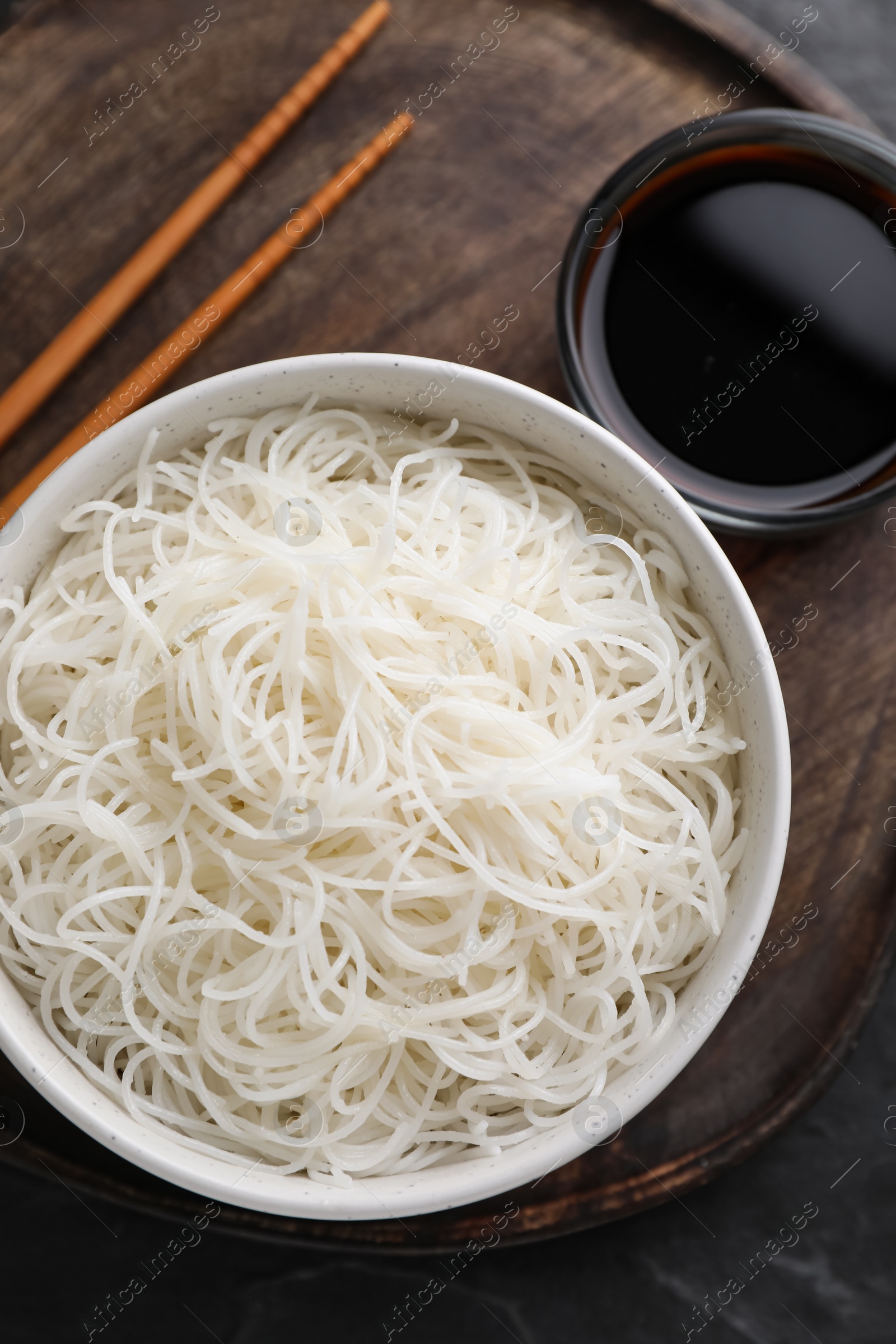 Photo of Bowl with cooked rice noodles, soy sauce and chopsticks on table, top view