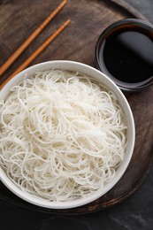 Bowl with cooked rice noodles, soy sauce and chopsticks on table, top view