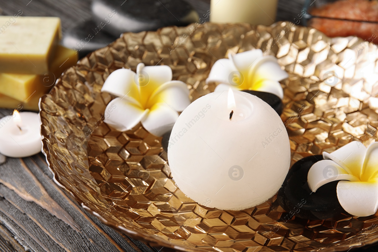 Photo of Candle, spa stones and flowers in plate with water on table