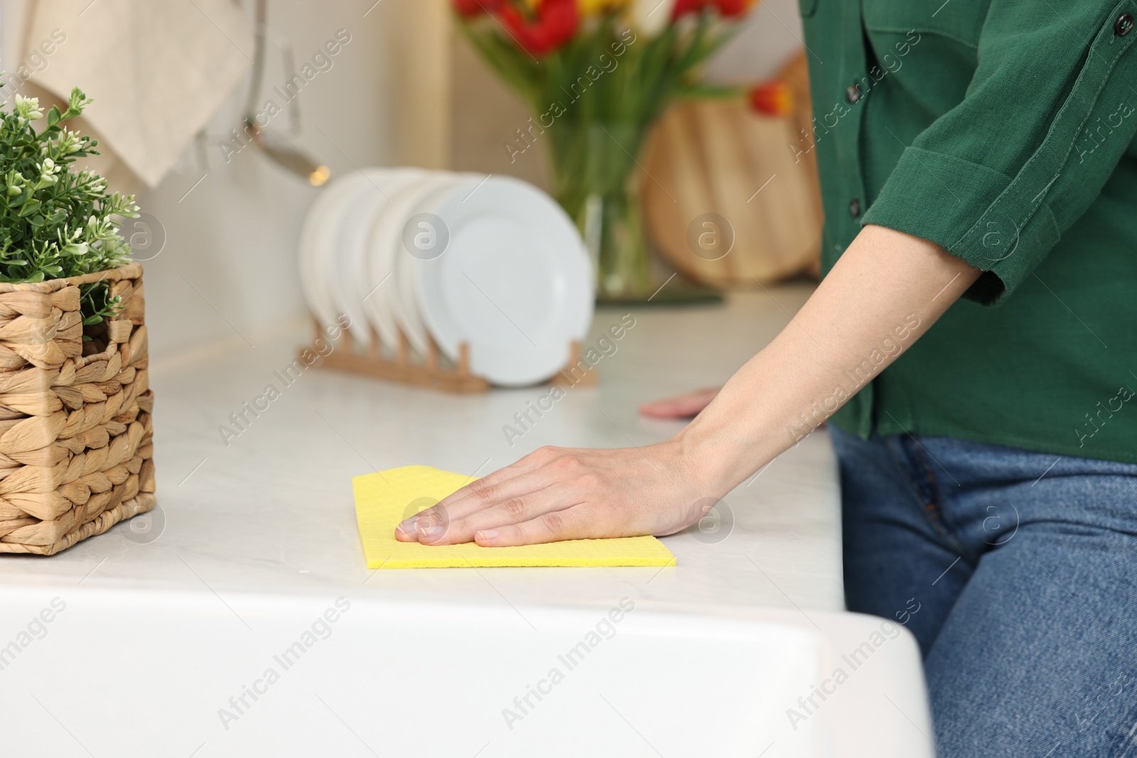 Photo of Woman cleaning table with sponge wipe in kitchen, closeup