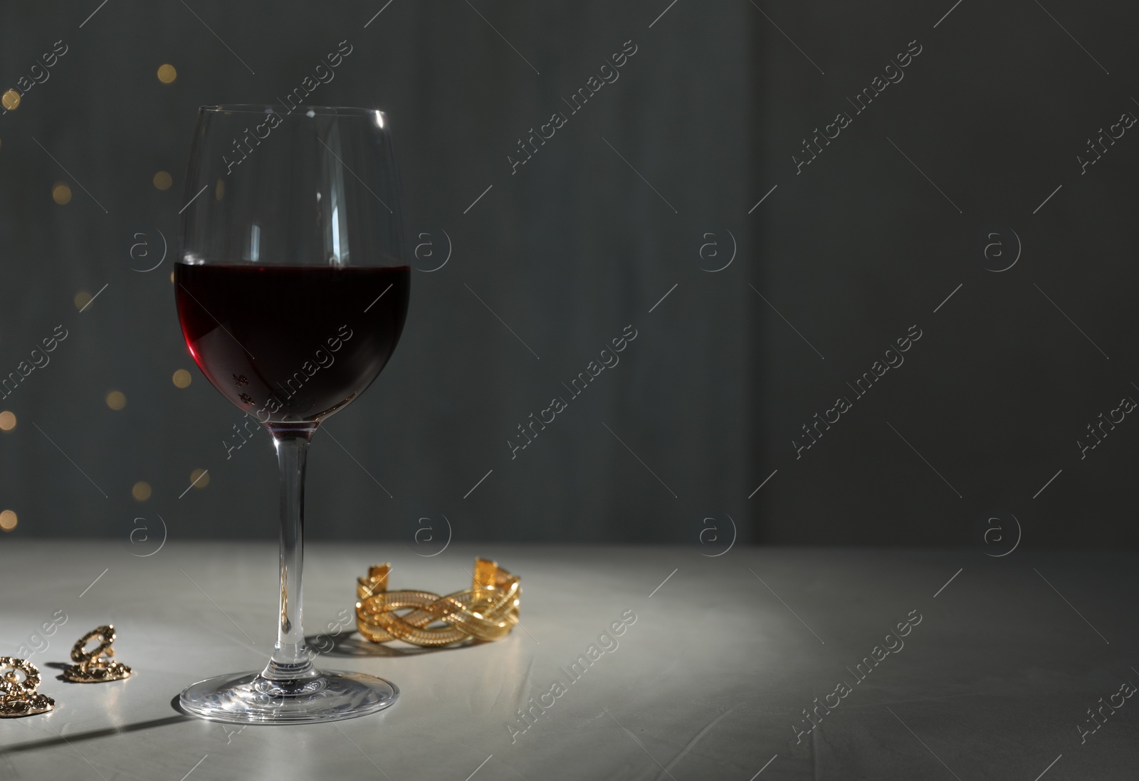 Photo of Glass of red wine and jewelry on white table against blurred festive lights, space for text