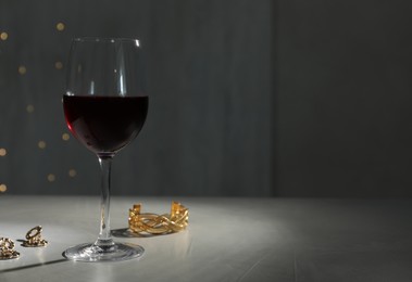 Glass of red wine and jewelry on white table against blurred festive lights, space for text