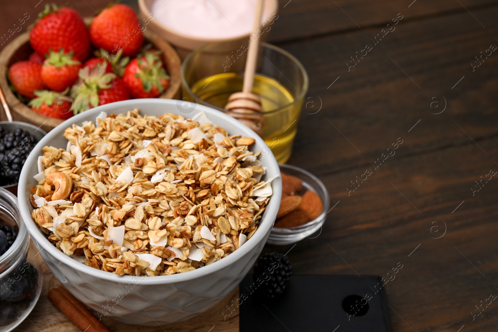 Photo of Tasty granola served with fresh berries, nuts and honey on wooden table, space for text. Healthy breakfast