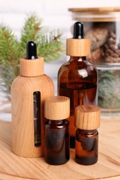 Photo of Bottles of essential oil, pine branches and cones on wooden board