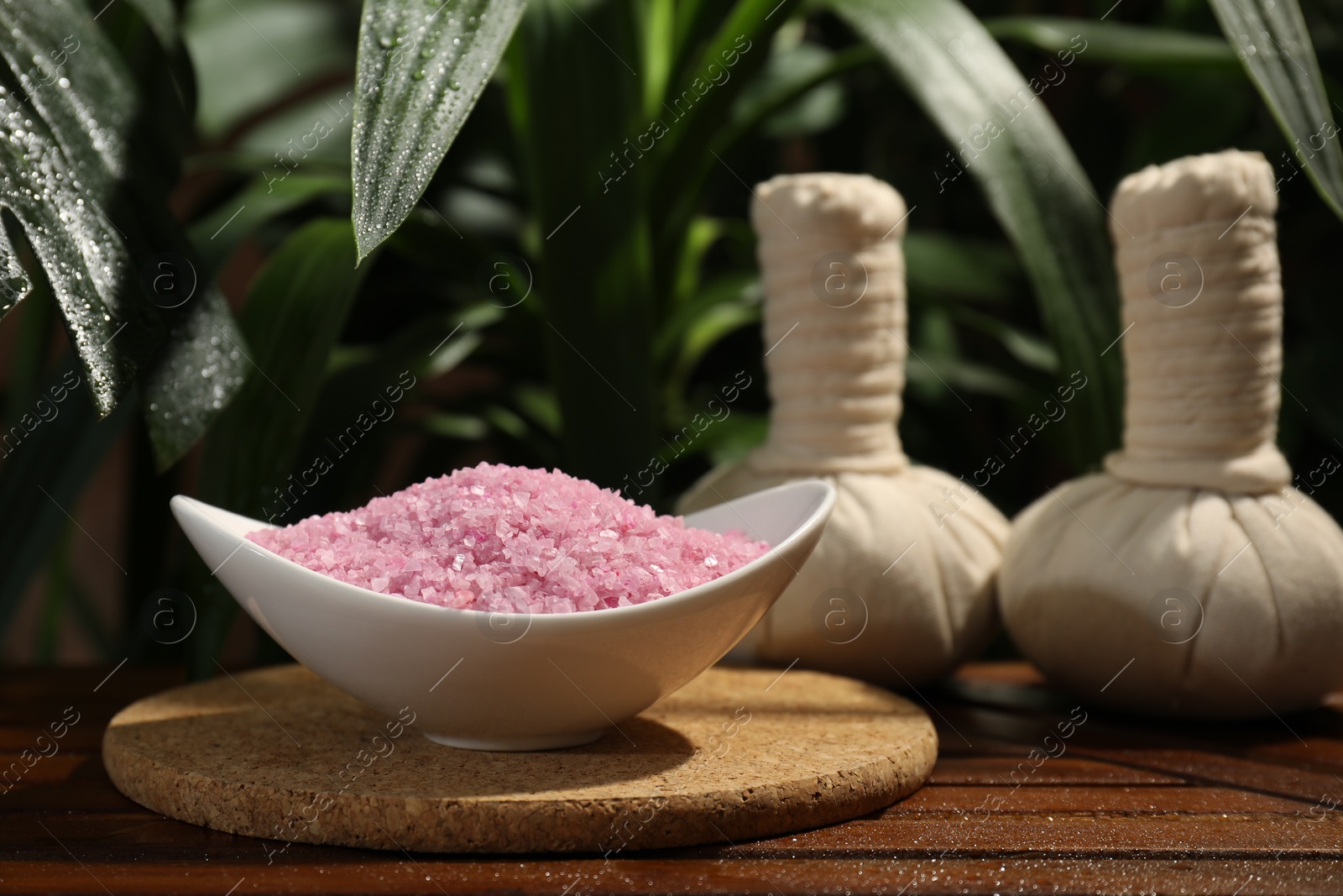 Photo of Bowl of pink sea salt and herbal massage bags on wooden table
