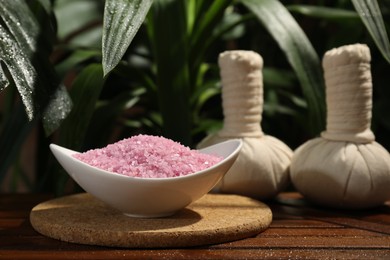 Bowl of pink sea salt and herbal massage bags on wooden table