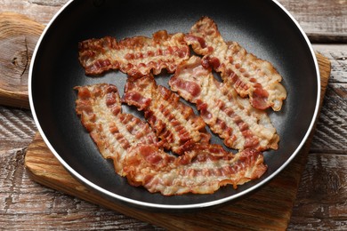 Photo of Delicious bacon slices in frying pan on wooden table, closeup