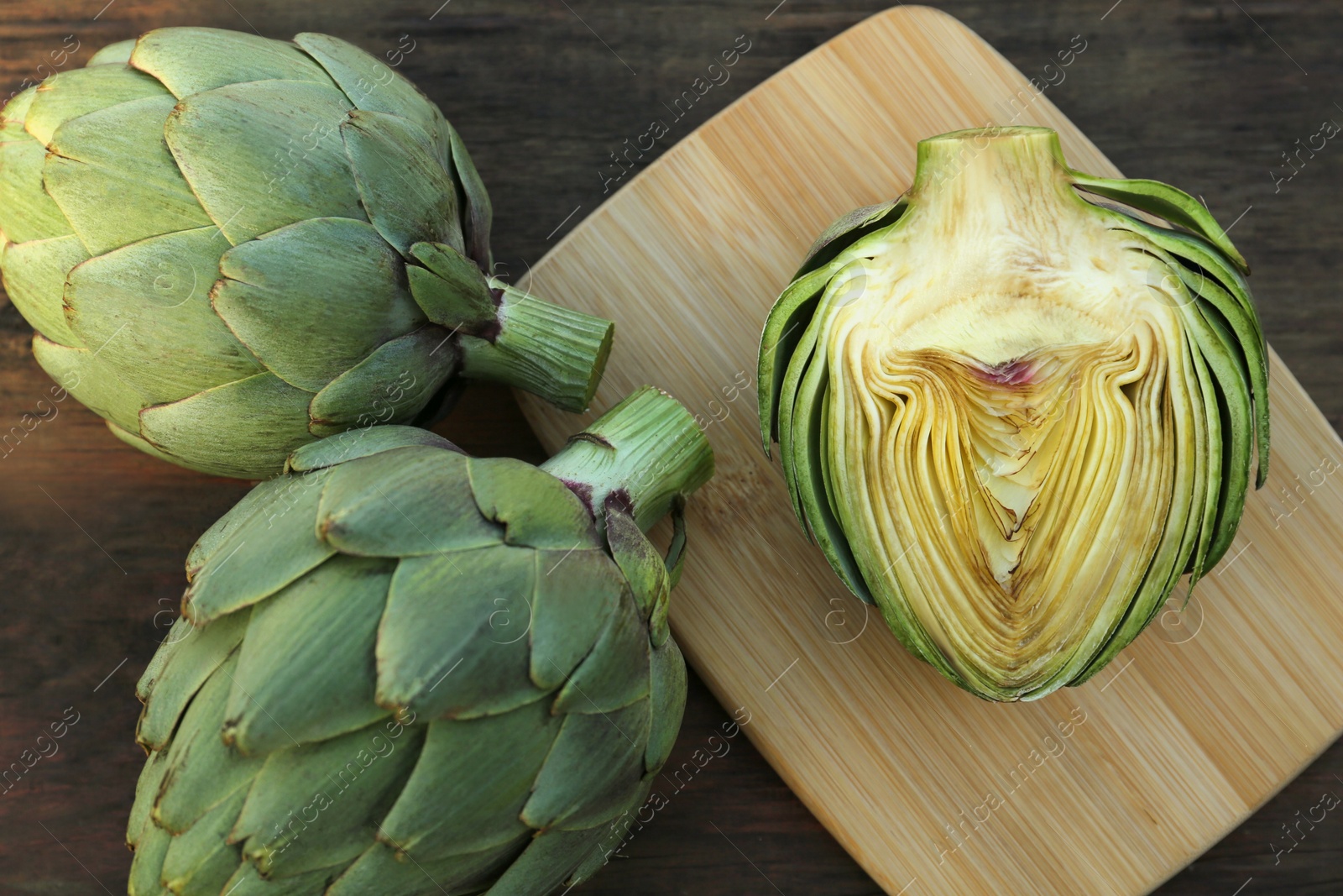 Photo of Whole and cut fresh raw artichokes on wooden table, flat lay