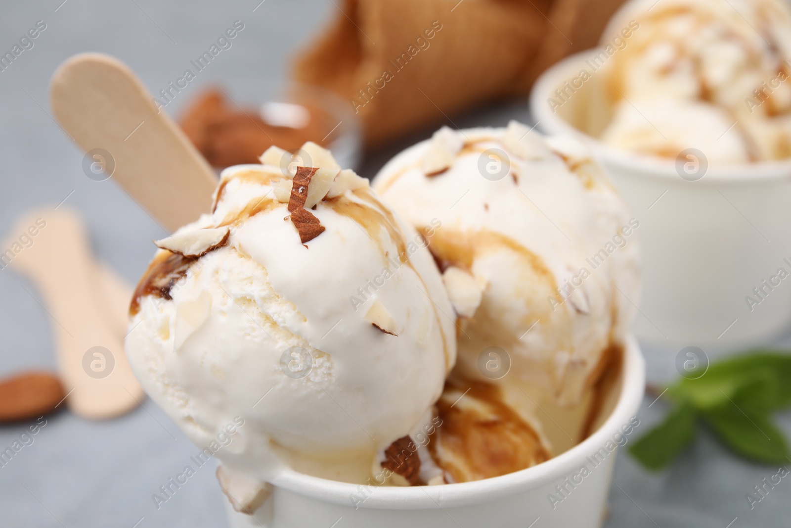 Photo of Scoops of ice cream with caramel sauce and nuts in paper cup, closeup