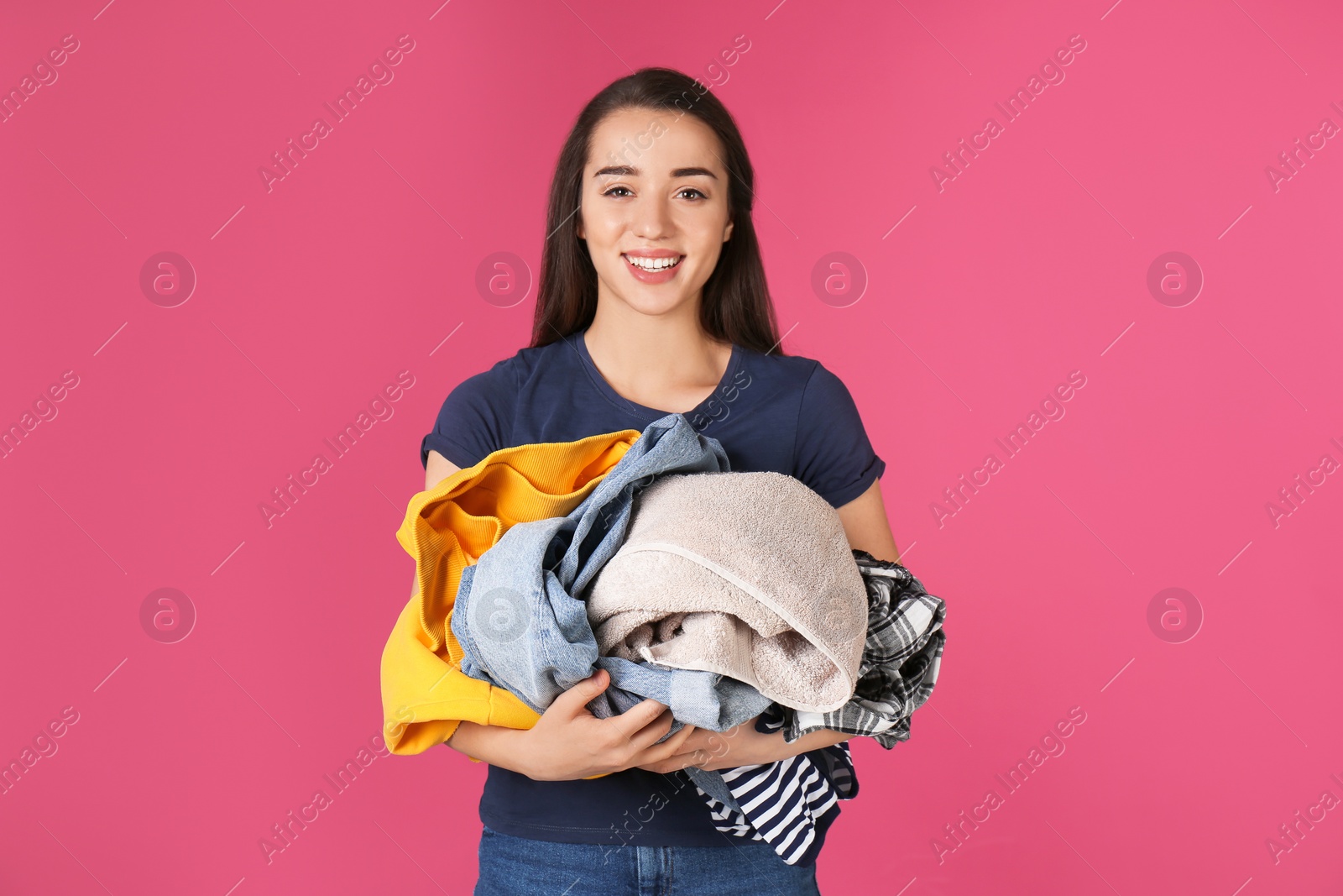 Photo of Happy young woman holding pile of dirty laundry on color background