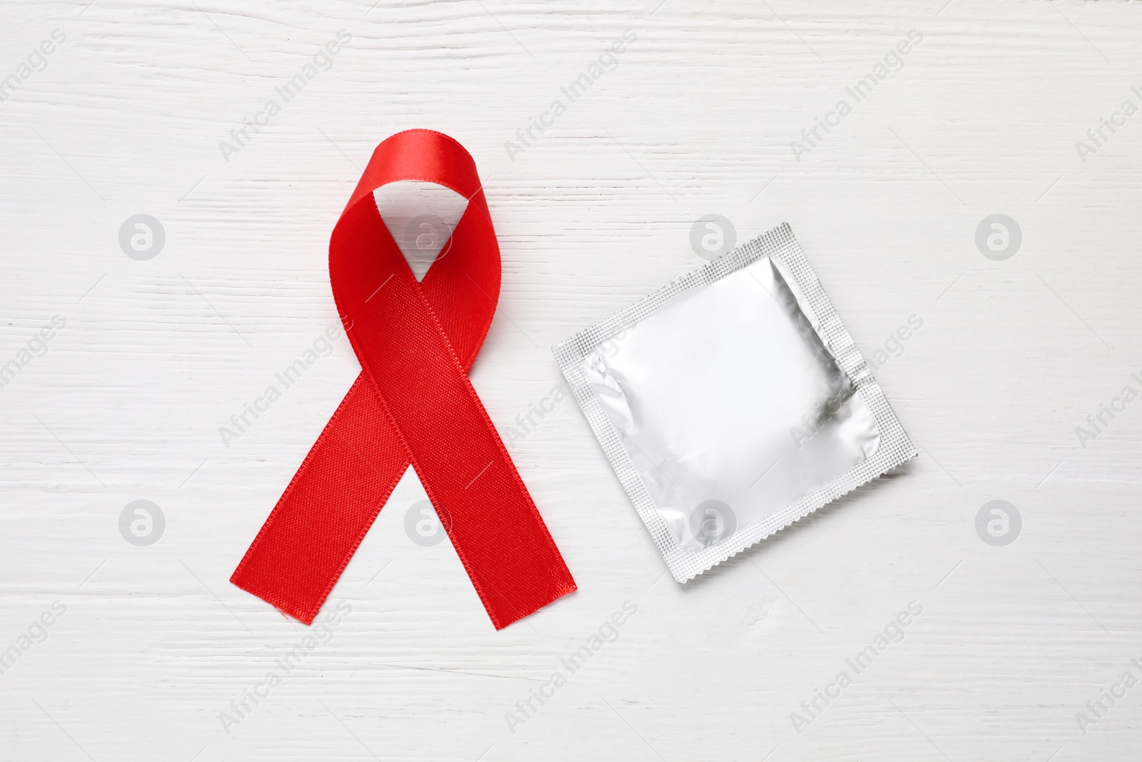 Photo of Red ribbon and condom on white wooden background, flat lay. AIDS disease awareness