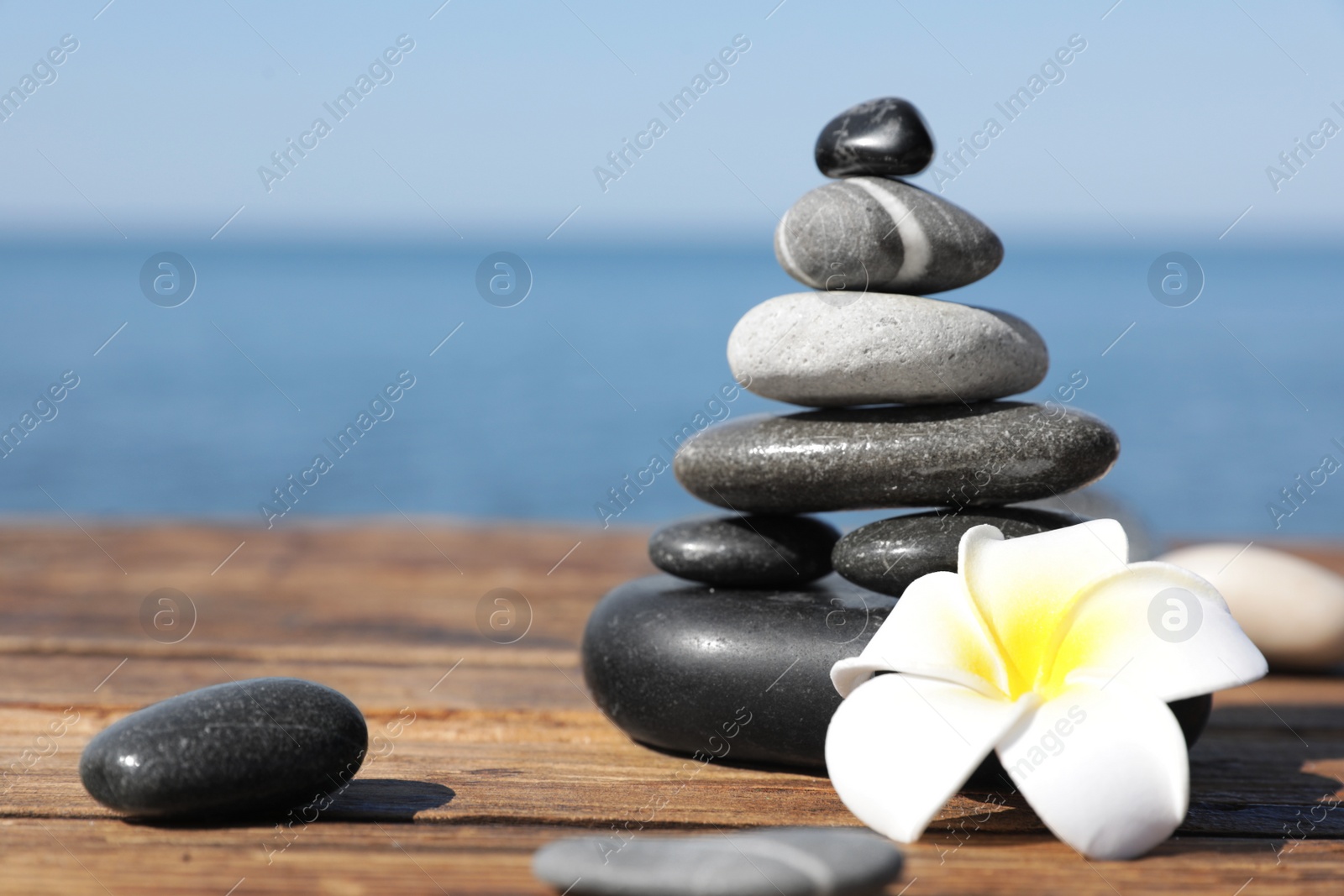 Photo of Stack of stones and flower on wooden pier near sea, space for text. Zen concept