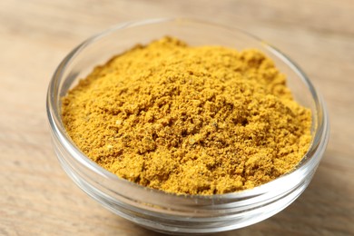 Photo of Curry powder in bowl on wooden table, closeup