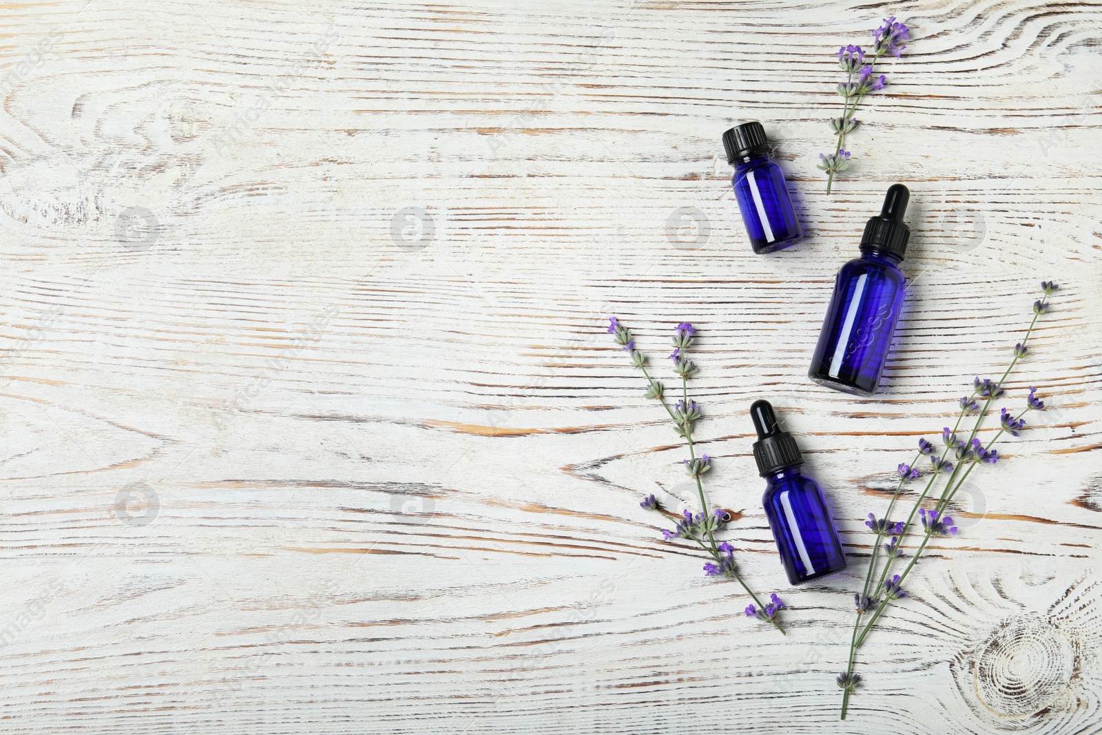 Photo of Bottles of essential oil and lavender flowers on white wooden background, flat lay. Space for text