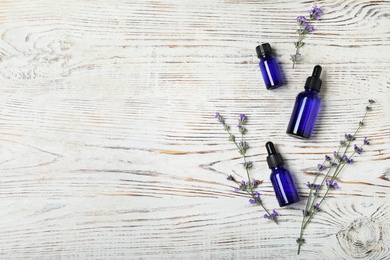 Photo of Bottles of essential oil and lavender flowers on white wooden background, flat lay. Space for text