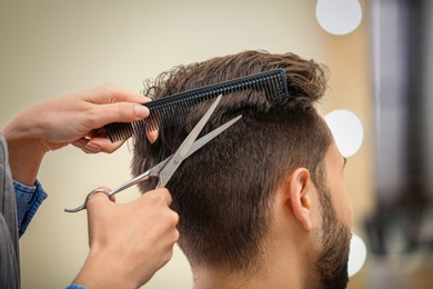 Barber making stylish haircut with professional scissors in beauty salon, closeup