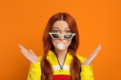 Photo of Portrait of beautiful woman in sunglasses blowing bubble gum on orange background