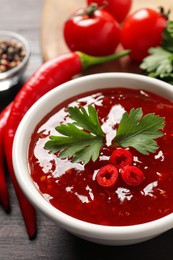 Photo of Spicy chili sauce with parsley on table, closeup