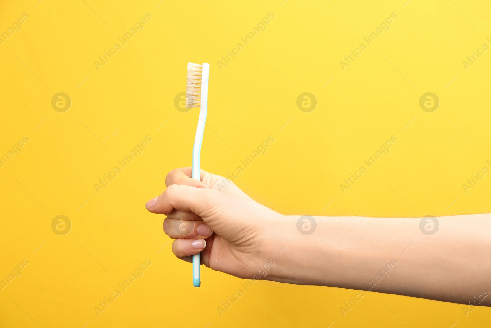 Photo of Woman holding toothbrush with natural bristles on yellow background, closeup