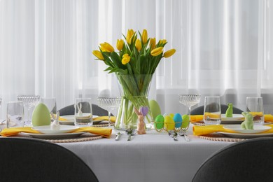 Festive table setting with glasses, painted eggs and vase of tulips. Easter celebration