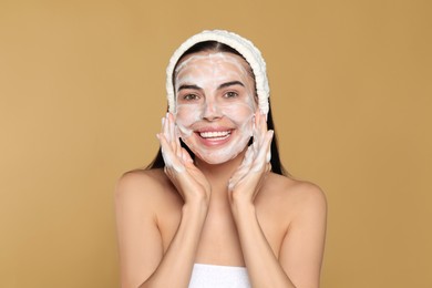 Photo of Happy young woman washing face with cosmetic product on beige background