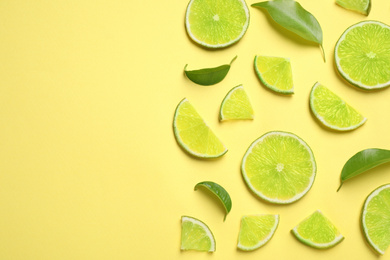 Photo of Juicy fresh lime slices and green leaves on yellow background, flat lay. Space for text