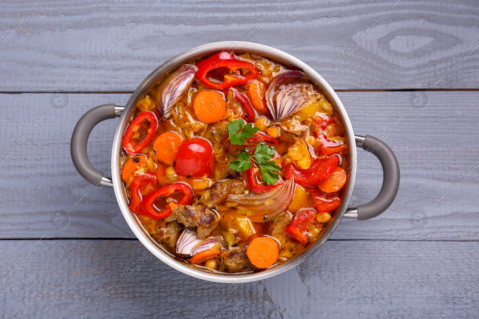 Photo of Saucepan of delicious vegetable soup with meat and ingredients on grey wooden table, top view