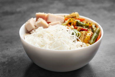 Photo of Tasty cooked rice noodles with chicken and vegetables on grey table