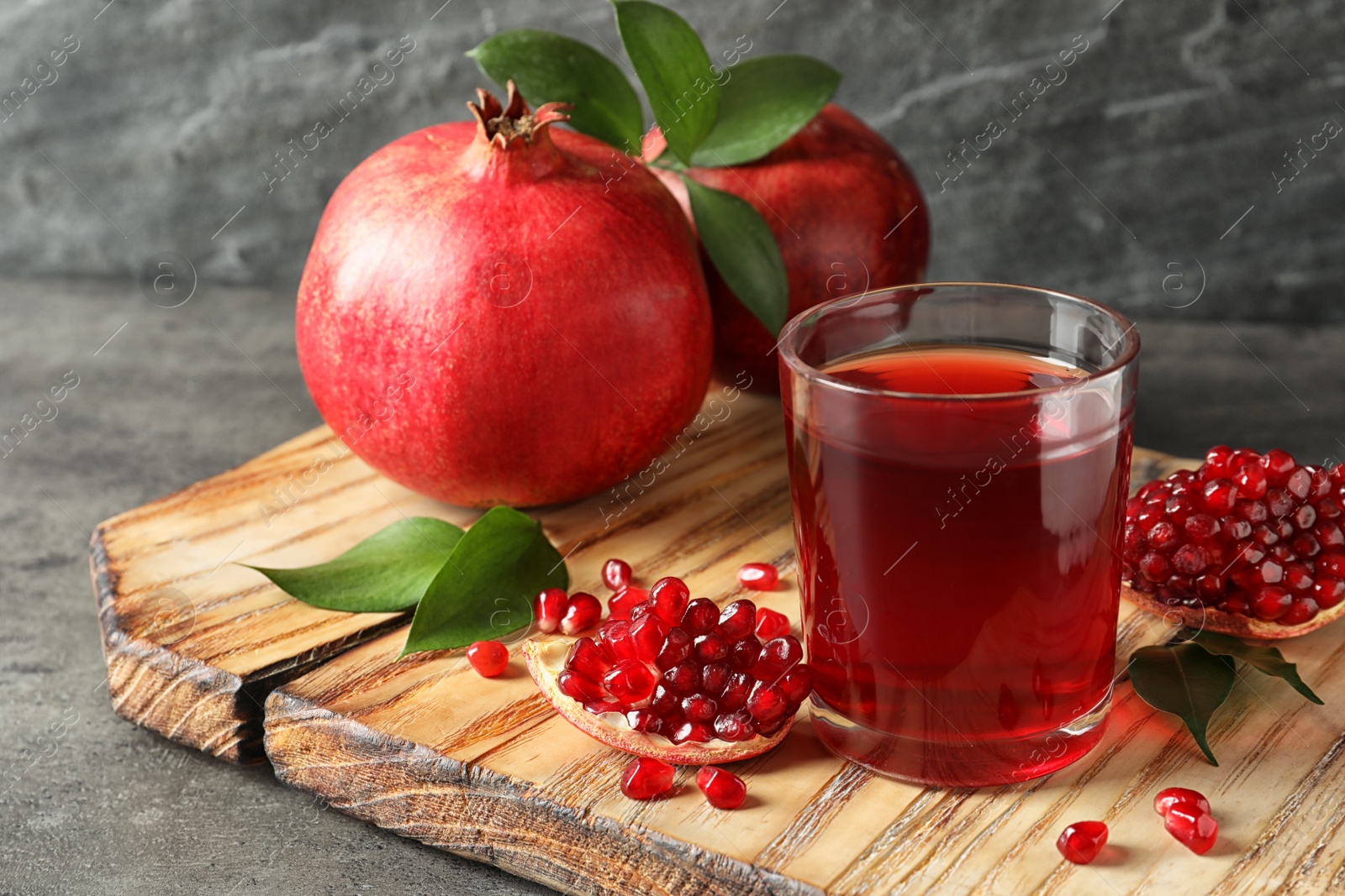 Photo of Glass of pomegranate juice and fresh fruits on wooden board against grey background