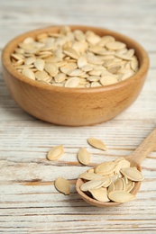 Photo of Raw unpeeled pumpkin seeds on white wooden table