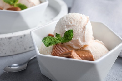 Bowl of ice cream with caramel candies and mint on light grey table, closeup