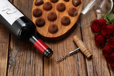 Photo of Red wine, chocolate truffles, corkscrew and roses on wooden table, closeup