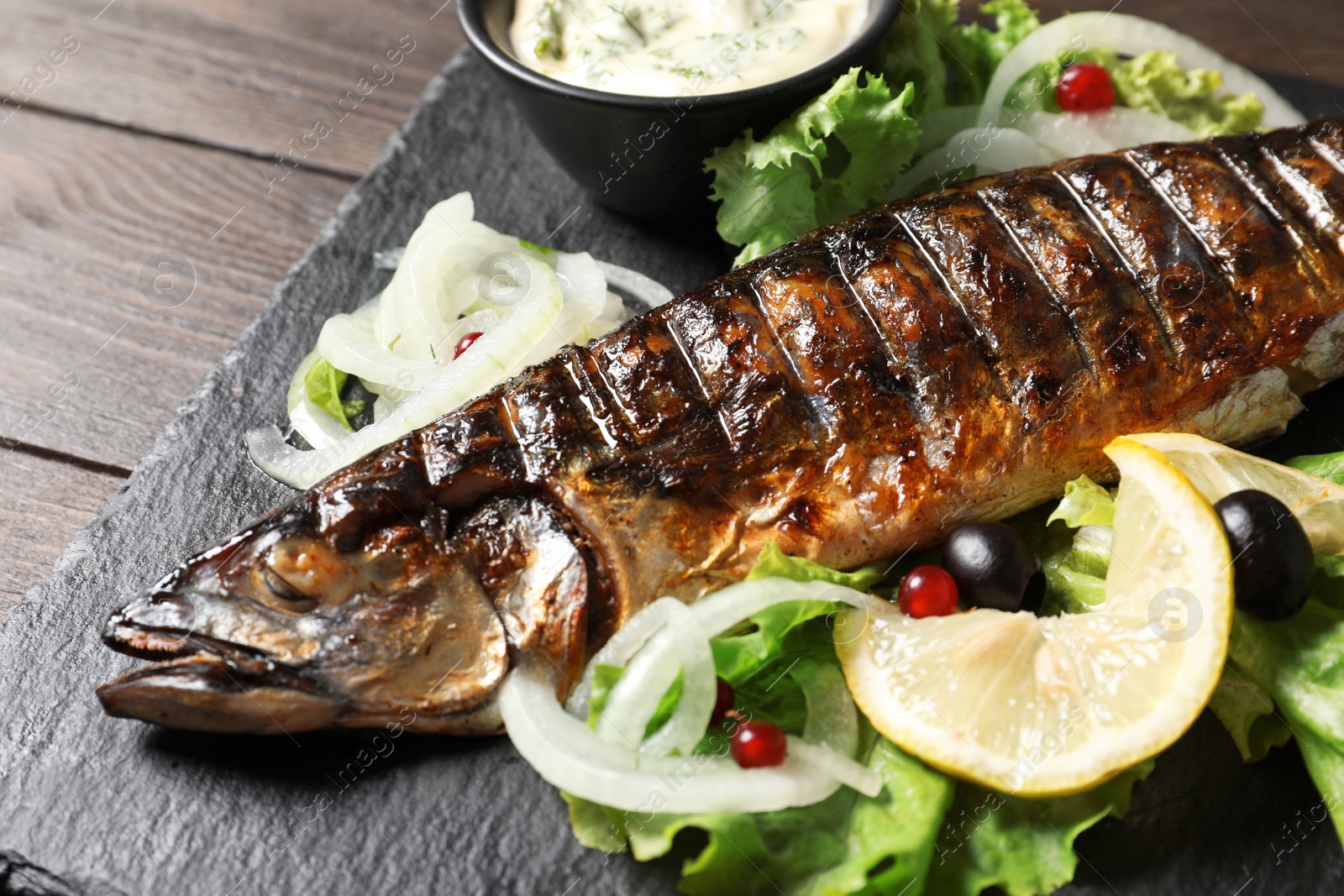 Photo of Slate plate with delicious grilled fish and sauce on table, closeup