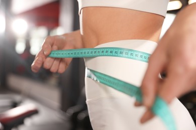 Photo of Slim woman measuring waist with tape in gym, closeup
