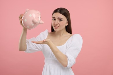 Sad woman with piggy bank on pink background