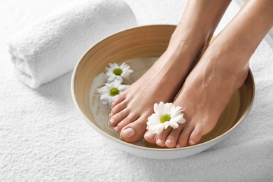 Photo of Closeup view of woman soaking her feet in dish with water and flowers on white towel, space for text. Spa treatment