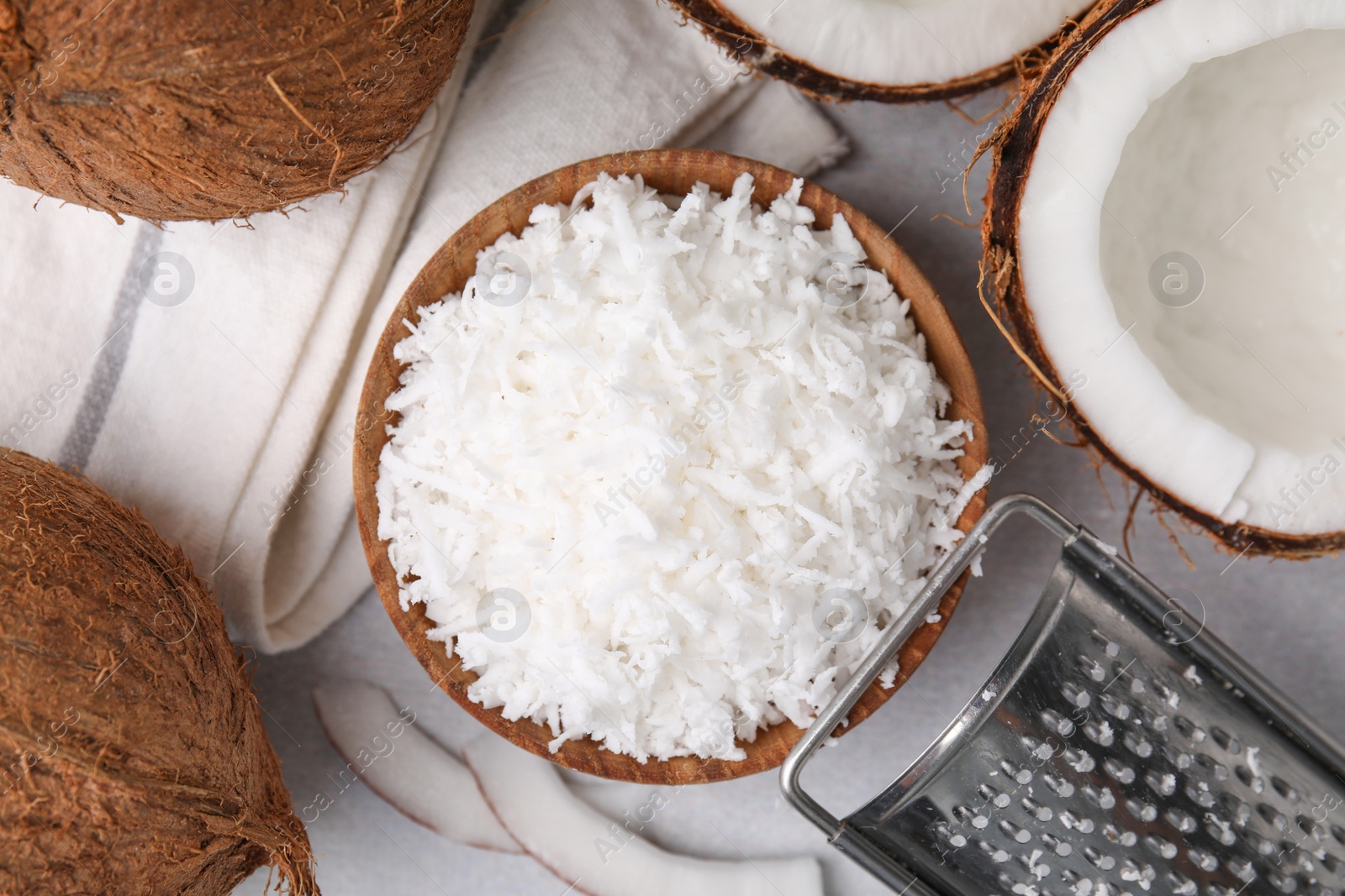 Photo of Coconut flakes in bowl, nuts and grater on light grey table, top view