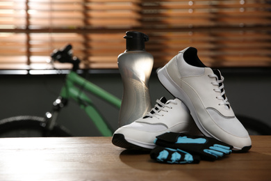 Photo of Bicycle gloves, shoes and bottle on wooden table indoors. Space for text