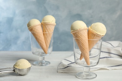 Photo of Delicious vanilla ice cream in waffle cones served on wooden table