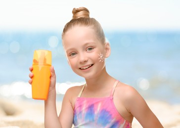 Image of Sun protection. Cute little girl with bottle of sunblock on beach