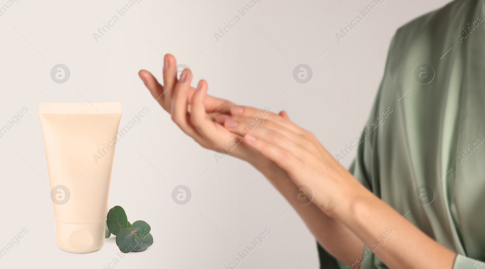 Image of Woman applying cream and tube of hand care cosmetic product on light background, closeup