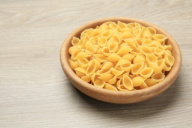 Photo of Raw conchiglie pasta in bowl on light grey wooden table, space for text