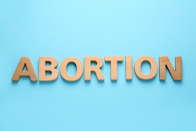 Photo of Word Abortion made of wooden letters on light blue background, flat lay