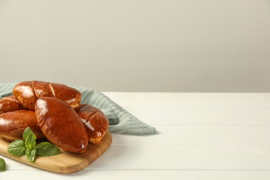 Photo of Delicious baked pirozhki and basil on white wooden table, space for text