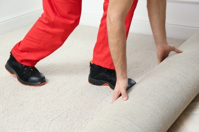 Worker rolling out new carpet flooring indoors, closeup