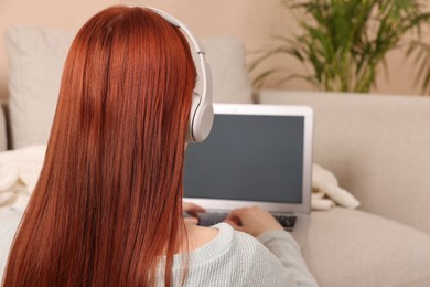 Photo of Woman with red dyed hair in headphone using laptop indoors
