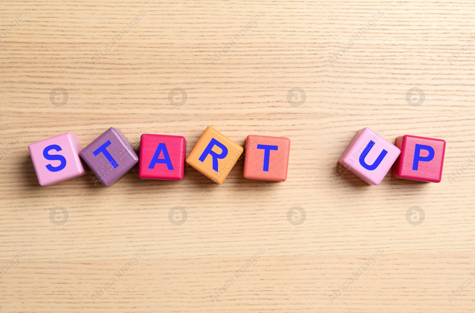 Photo of Words START UP made with color cubes on wooden background, flat lay