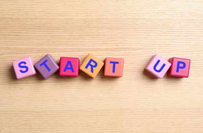Words START UP made with color cubes on wooden background, flat lay