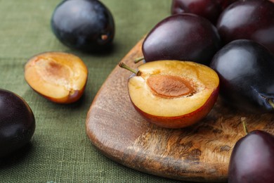 Many tasty ripe plums and wooden board on green fabric, closeup