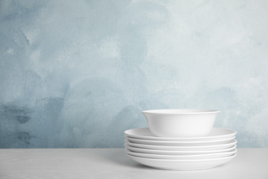 Photo of Stack of clean plates and bowl on white table against light blue background. Space for text